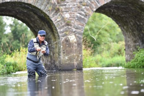 Fly fisherman fishing in river to catch brown trout
