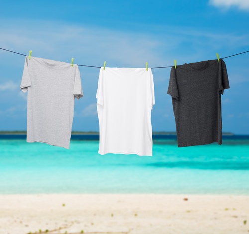Close up of a dark grey, white and grey t-shirts on the rope. Tropical sand beach and ocean as background. deodorant that doesn't stain